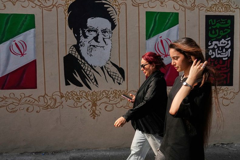 Dos mujeres caminan frente a una imagen del difunto líder supremo de Irán, ayatolá Ali Jamenei, quien fue abatido en un ataque de Estados Unidos e Israel, el jueves 20 de agosto de 2026, en el centro de Teherán, Irán. (AP Foto/Vahid Salemi)