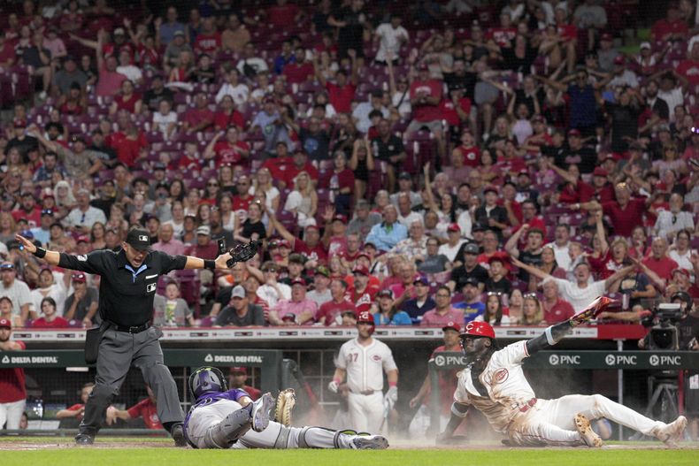 Elly De La Cruz, derecha, de los Rojos de Cincinnati, reacciona después de evitar un toque del receptor de los Rockies de Colorado, Elias Díaz, centro, y anotar en jugada de opción después de un batazo de Jeimer Candelario durante la octava entrada del juego de béisbol del lunes 8 de julio de 2024, en Cincinnati. (AP Foto/Jeff Dean)