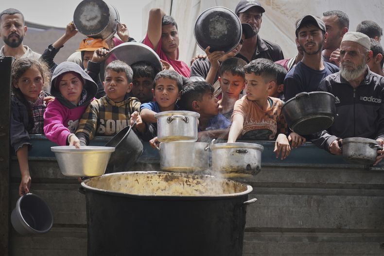 Niños y adultos palestinos esperan para recibir comida en una cocina comunitaria en Jan Yunis, en el sur de la Franja de Gaza, el jueves 24 de abril de 2025. (AP Foto/Abdel Kareem Hana)