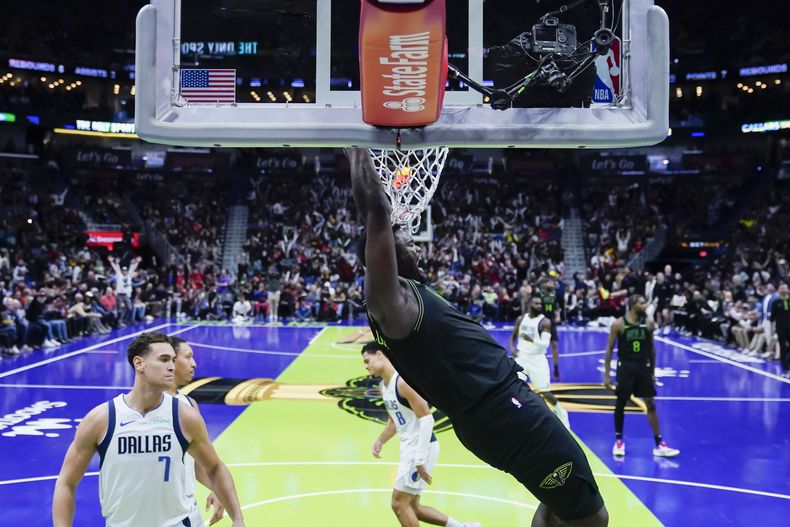 Zion Williamson, de los Pelicans de Nueva Orleáns, cuelga del aro tras realizar una clavada ante Dwight Powell (7), de los Mavericks de Dallas, el martes 14 de noviembre de 2023 (AP Foto/Gerald Herbert)