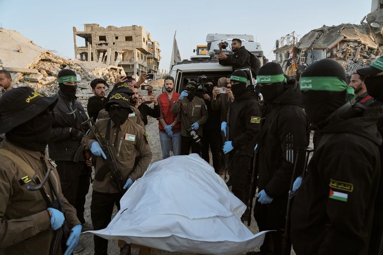 Miembros de los grupos Yihad Islámica y Hamás, con el rostro enmascarado, entregan una bolsa que se cree que contiene los restos de un rehén fallecido a la Cruz Roja, para su traspaso a las autoridades israelíes, en Beit Lahiya, en el norte de la Franja de Gaza, el 3 de diciembre de 2025. (AP Foto/Jehad Alshrafi)