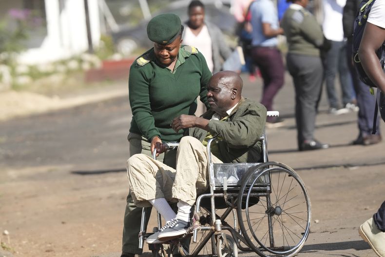 Una agente penitenciaria acompaña a un preso mayor, que va en silla de ruedas, tras ser liberado en una cárcel en Harare, Zimbabue, el 19 de mayo de 2023. (AP Foto/Tsvangirayi Mukwazhi)