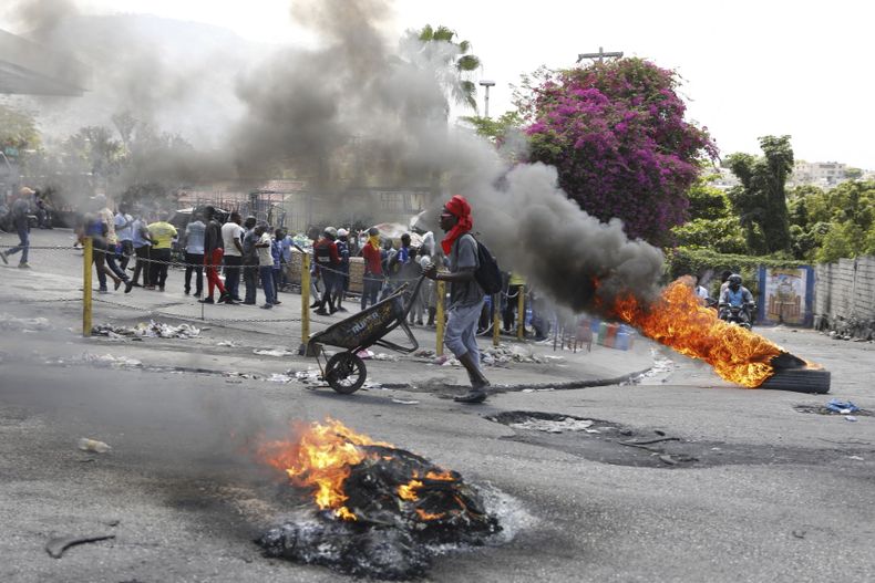 Un hombre empuja una carretilla frente a neumáticos en llamas durante una protesta para exigir la renuncia del primer ministro Ariel Henry, el jueves 7 de marzo de 2024, en Puerto Príncipe, Haití. (AP Foto/Odelyn Joseph)