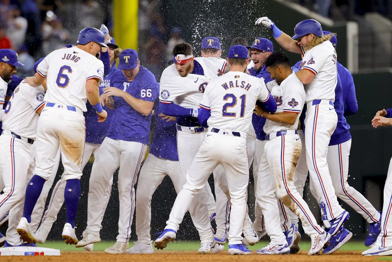 Jonah Heim, centro, de los Rangers de Texas, y sus compañeros de equipo celebran el sencillo de Heim que impulsó la victoria contra los Cachorros de Chicago en la décima entrada del juego de béisbol el jueves 28 de marzo de 2024 en Arlington, Texas. (AP Foto/Gareth Patterson)
