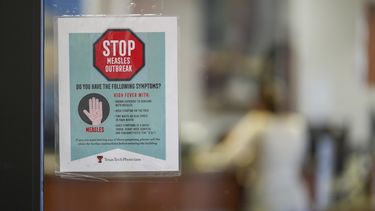Un letrero de advertencia sobre el sarampión en una puerta de cristal, mientras una paciente llega a una cita en el área de medicina familiar en Texas Tech Physicians of the Permian Basin, el lunes 24 de febrero de 2025, en Odessa, Texas. (AP Foto/Julio Cortez)