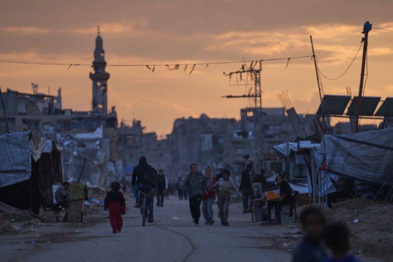 Jóvenes palestinos caminan entre en un campamento para desplazados al atardecer, el viernes 26 de diciembre de 2025, en Nuseirat, en Franja de Gaza. (AP Foto/Abdel Kareem Hana)