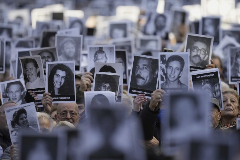 ARCHIVO - La gente sostiene fotografías de víctimas del atentado mientras suenan las sirenas durante una ceremonia que conmemora el 30º aniversario del ataque contra el centro judío AMIA que mató a 85 personas, en Buenos Aires, Argentina, el 18 de julio de 2024. (AP Foto/Natacha Pisarenko, Archivo)