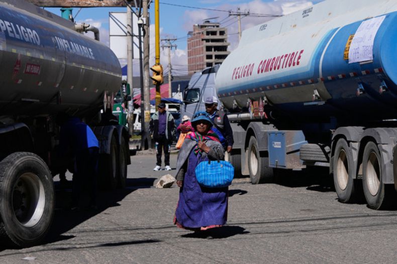 Una mujer pasa junto a unos camiones cisterna que bloquean una carretera durante una huelga provocada por la escasez de gasóleo en El Alto, Bolivia, el lunes 27 de abril de 2026. (Foto AP/Juan Karita)