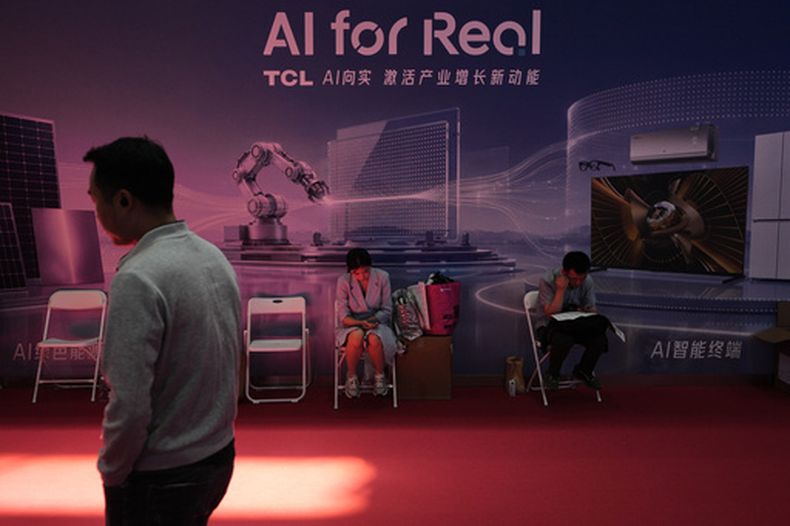 Un hombre pasa por delante de trabajadores descansando en un puesto de promoción de la Inteligencia Artificial (AI, por sus siglas en inglés) en la China International Supply Chain Expo en Beijing, el 25 de junio de 2026. (AP Foto/Andy Wong)
