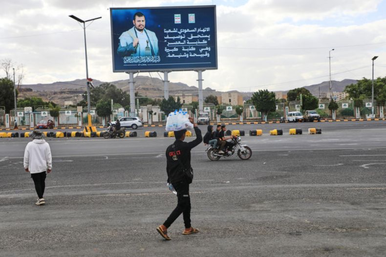 Un vendedor pasa bajo un cartel con la imagen del líder hutí Abdul Malik al-Houthi y la frase la acusación saudí contra nuestra gente merece describirse como la mentira del siglo, en Saná, Yemen, el lunes 5 de octubre de 2026. (AP Foto/Osamah Abdulrahman)