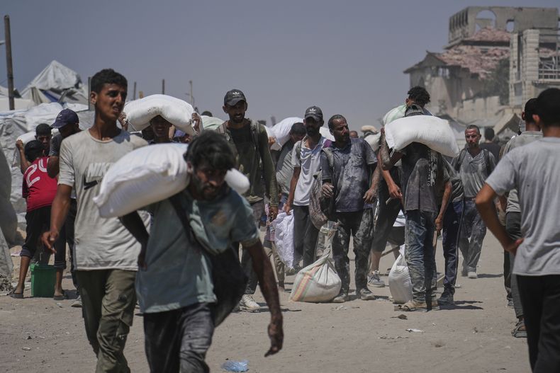 Palestinos cargan sacos de harina descargados por un convoy de ayuda humanitaria que llegó a Ciudad de Gaza desde el norte de la Franja de Gaza, el domingo 27 de julio de 2025. (AP Foto/Abdel Kareem Hana)