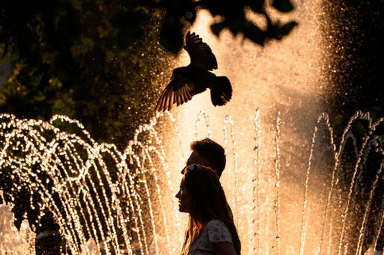 Una pareja pasa por una fuente pública en un día caluroso, en el que la agencia Nacional de Meteorología emitió una alerta roja por calor extremo en partes del país, en Bucarest, Rumanía, el sábado 27 de junio de 2026. (AP Foto/Andreea Alexandru)