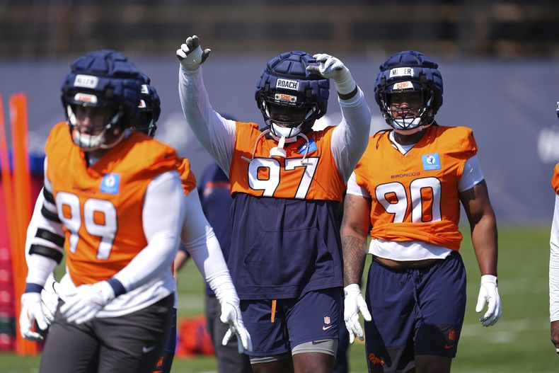 El tackle defensivo de los Broncos de Denver, Malcolm Roach, en el centro, levanta los brazos para agradecer el aplauso de los aficionados mientras calienta entre el ala defensiva Zach Allen, al frente, y el tackle defensivo Jordan Miller durante una práctica de fútbol americano de la NFL el viernes 25 de julio de 2025, en Centennial, Colorado. (AP Photo/David Zalubowski)