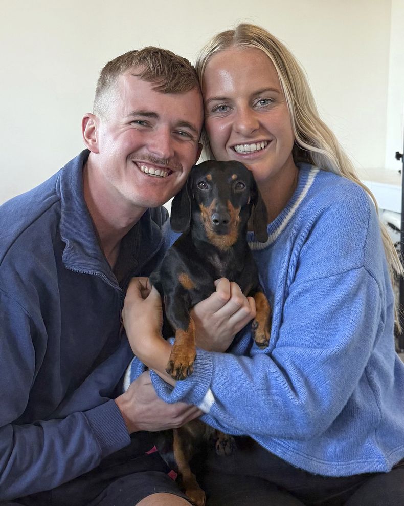 Georgia Gardner y su pareja, Josh Fishlock, posan sosteniendo en brazos a Valerie, su perro salchicha, tras reunirse en Isla Canguro, en el sur de Australia, luego de que el animal estuvo 540 días desaparecido, el 6 de mayo de 2025. (Ruby Stewart/The Advertiser vía AP)