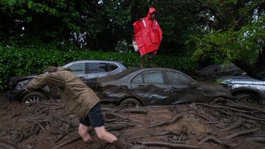 Un hombre está de pie sobre el techo de un automóvil mientras otro camina por aguas lodosas tras las fuertes lluvias que provocaron inundaciones repentinas en la comuna de Las Condes, en Santiago de Chile, el jueves 8 de octubre de 2026. (Foto AP/Esteban Félix)