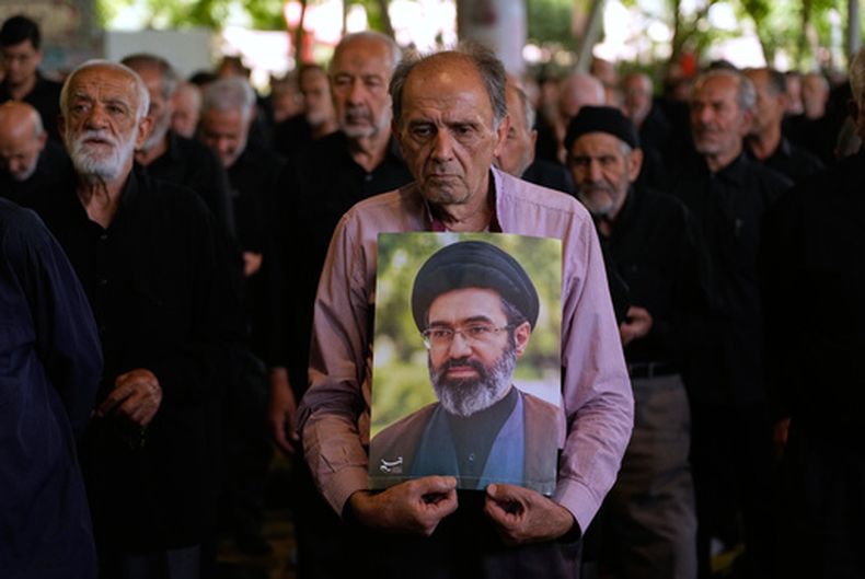Fieles iraníes escuchan un sermón en la oración del viernes mientras uno de ellos sostiene un cartel con la imagen del líder supremo del país, el ayatolá Moytabá Jamenei, en el campus de la Universidad de Teherán, en Teherán, Irán, el 19 de junio de 2026. (AP Foto/Vahid Salemi)