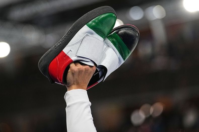 El italiano Mattia Giovanella hace un gesto sosteniendo sus zapatos, tras la sesión de la ronda preliminar masculina de curling contra Gran Bretaña, en los Juegos Olímpicos de Invierno de 2026, en Cortina dAmpezzo, Italia, el viernes 13 de febrero de 2026. (AP Photo/Fatima Shbair)