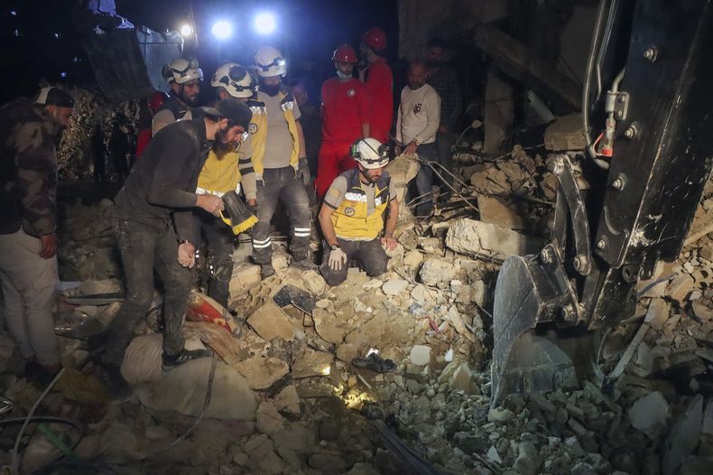 En esta imagen proporcionada por la Defensa Civil Siria, miembros del grupo, conocidos como Cascos Blancos, buscan entre los restos de un edificio de cuatro plantas tras la explosión de municions de la guerra de 13 años en Siria en la ciudad costera de Latakia, Siria, la mañana del domingo 16 de marzo de 2025. (Defensa Civil Siria/Cascos Blancos via AP)