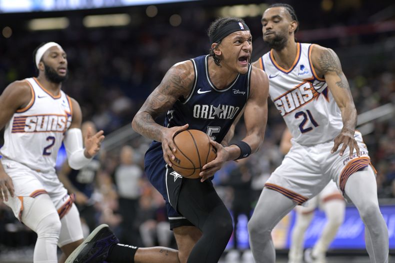 El alero del Magic de Orlando Paolo Banchero avanza hacia la canasta mientras lo defiende el alero de los Suns de Phoenix Keita Bates-Diop y Josh Okogie observa en el encuentro de la NBA del domingo 28 de enero del 2024. (AP Foto/Phelan M. Ebenhack)