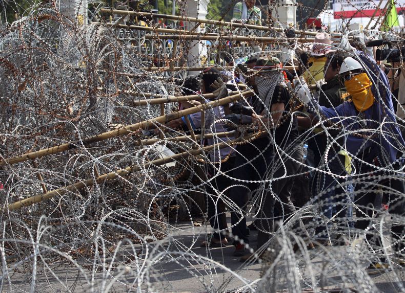 Manifestanes antigubernamentales usan una escalera para tratar de quitar el alambre de p&uacute;as colocado a la entrada de las oficinas de la primera ministra en  Bangkok, Tailand&iacute;a, el jueves 12 de diciembre de 2013. (Foto AP/Sakchai Lalit)