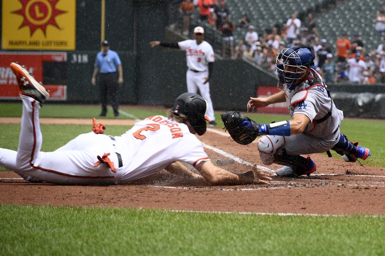 Gunnar Henderson de los Orioles de Baltimore se lanza al plato frente al catcher de Los Ángeles Austin Barnes tras el doble anotador del mexicano Ramón Urías en el encuentro del miércoles 19 de julio del 2023. (AP Foto/Nick Wass)