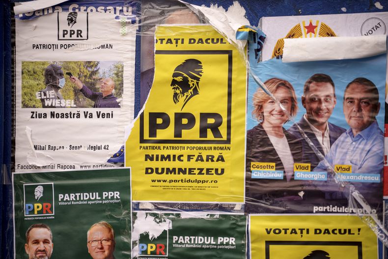Carteles de varios partidos políticos, uno de ellos con un hombre apuntando con un termómetro a una estatua de Ellie Wiesel y con la leyenda Nuestro día llegará, colocados en un panel antes de las elecciones parlamentarias del 1 de diciembre en Bucarest, Rumanía, jueves 28 de noviembre de 2024. (AP foto/Andreea Alexandru)
