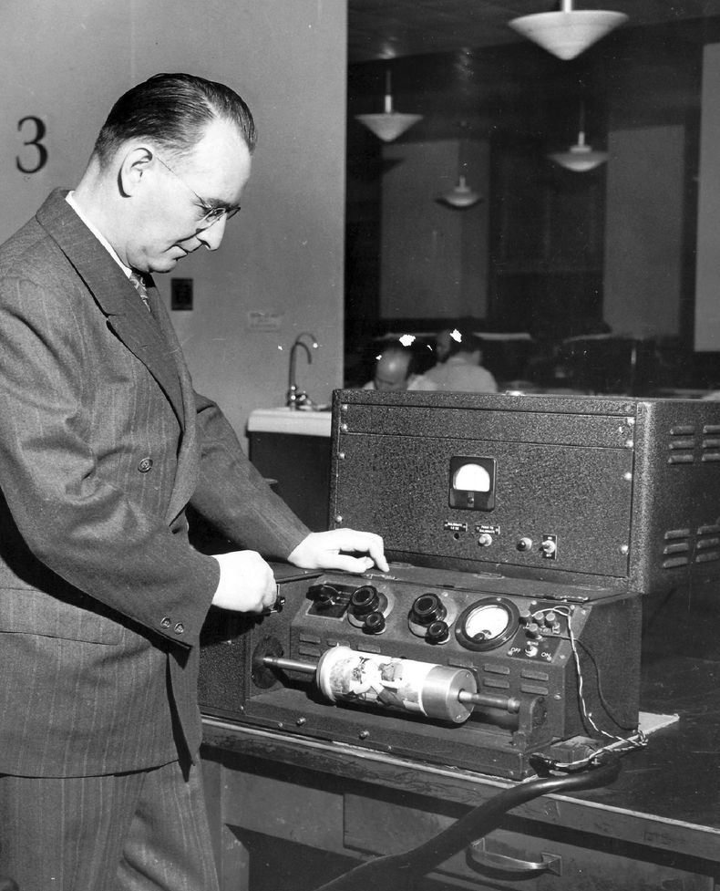 El operador de AP Wirephoto Harold King muestra el equipo de transmisión de fotografías las oficinas centrales de The Associated Press en Nueva York, alrededor de 1950. AP reunirá un pequeño ejército para cubrir la coronación del rey Carlos III este fin de semana. Para la coronación de su madre hace 70 años, el servicio de noticias también contó con la ayuda de una fuerza aérea. En 1953, tomaba ocho minutos transmitir una sola fotografía en blanco y negro, siempre que las condiciones climáticas y las líneas telefónicas cooperaran. Entre los métodos que AP empleó para transmitir las fotos de Londres a sus clientes de periódicos estadounidenses había un acuerdo para ponerlas en aviones de combate de la Fuerza Aerea Real. (Foto AP/Archivos Corporativos)