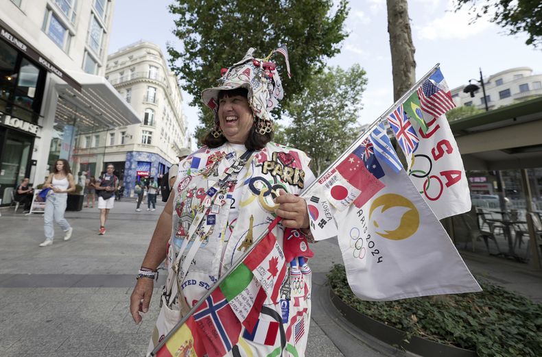 La estadounidense Vivianne Robinson, quien asiste a sus séptimos Juegos Olímpicos como aficionada en París, posa con sus numerosos pines, banderas e insignias, el martes 30 de julio de 2024 (AP Foto/Lujain Jo)
