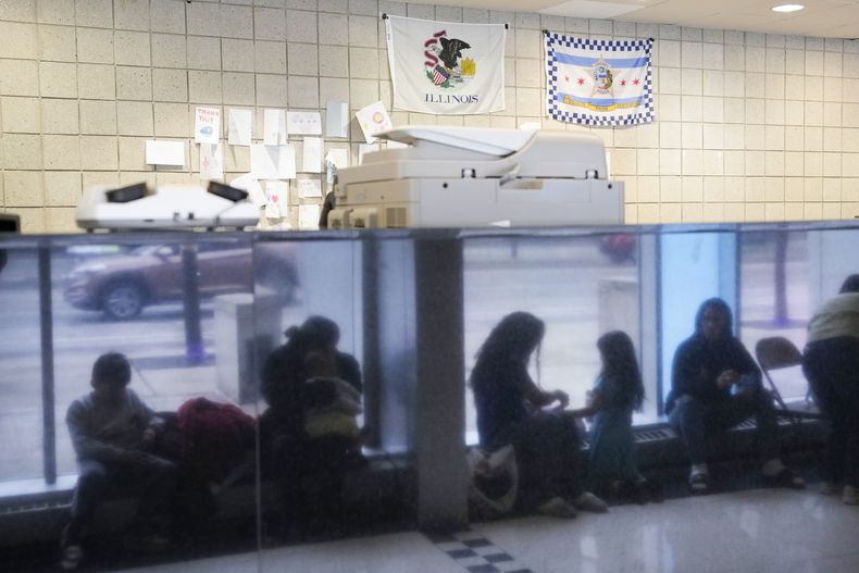 ARCHIVO - Migrantes procedentes de Venezuela se ven reflejados en una pared de mármol mientras encuentran refugio en la comisaría del distrito 16 del Departamento de Policía de Chicago el 1 de mayo de 2023. (AP foto/Charles Rex Arbogast, archivo)