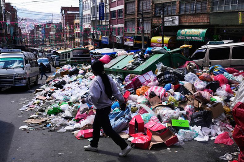 Una mujer camina junto a la basura esparcida por la calle durante una huelga de recolectores de basura que exigen mayores tarifas de recolección para compensar el aumento de los costos de combustible y mano de obra en La Paz, Bolivia, el martes 25 de agosto de 2026. (Foto AP/Juan Karita)