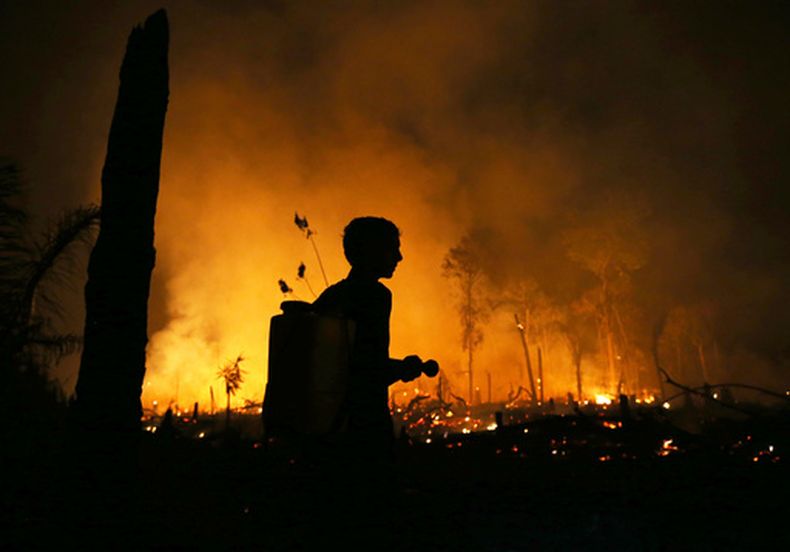 Un residente con una linterna observa los incendios forestales que arden en el municipio de Autazes, en el estado de Amazonas, Brasil, el lunes 12 de octubre de 2026. (AP Foto/Edmar Barros)