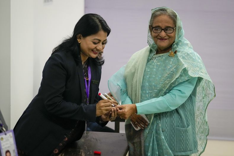 Una policía de Bangladesh pone tinta indeleble en el dedo de la primera ministra del país, Sheikh Hasina, a su llegada para votar en Daca, Banfladesh, el domingo 7 de enero de 2024. (AP Foto/Altaf Qadri)