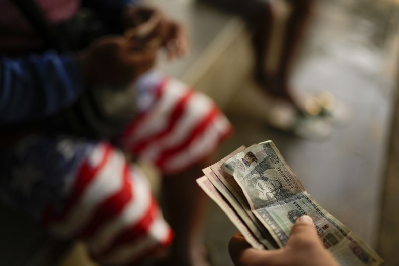 Gerzon Zavala, que migró desde Honduras, cambia quetzales guatemaltecos por pesos mexicanos tras cruzar el río Suchiate, fronterizo entre Guatemala y México, desde Ciudad Hidalgo, México, el lunes 28 de octubre de 2024. (AP Foto/Matías Delacroix)