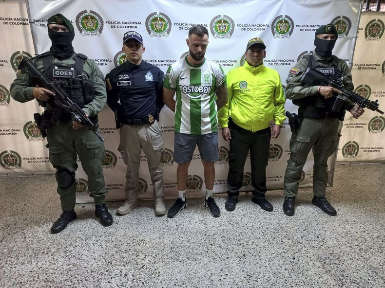 Esta fotografía publicada por la Oficina de Prensa de la Policía Nacional de Colombia muestra a quien identifican como el ciudadano británico Christopher Neil, conocido con el alias Dips, en el centro, tal como lo muestran a la prensa en Medellín, Colombia, el viernes 13 de diciembre de 2024. Colombia ha capturado al presunto narcotraficante británico que supuestamente se convirtió en el coordinador del cártel colombiano Clan del Golfo para el tráfico de cocaína al Reino Unido, según la policía. (Oficina de Prensa de la Policía Nacional de Colombia vía AP)