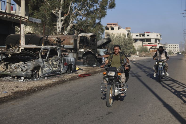 Combatientes beduinos en motocicleta pasan junto a vehículos quemados en la localidad de Mazraa,a las afueras de la ciudad de Sweida, en el sur de Siria, el sábado 19 de julio de 2025. (AP Foto/Ghaith Alsayed)