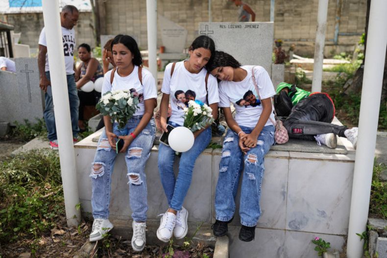 Noemi Marrero (izquierda) y sus hermanas, sentadas en un cementerio en La Guaira, Venezuela, durante el funeral por los dos hijos de Marrero, que murieron en los sismos, el 17 de agosto de 2026. (AP Foto/Ariana Cubillos)