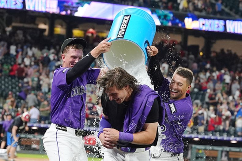 TJ Rumfield, izquierda, y Tyler Freeman, derecha, de los Rockies de Colorado, bañan a Jake McCarthy, centro, después del triple de tres carreras de McCarthy para dejar tendidos en el terreno a los Medias Rojas de Boston en el juego de béisbol de Grandes Ligas, el lunes 22 de junio de 2026, en Denver. (AP Foto/David Zalubowski)