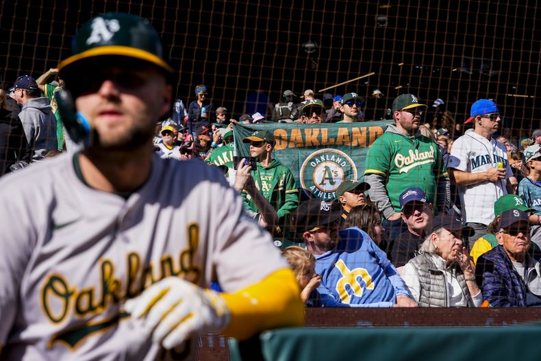 Un fanático despliega un banderín de los Atléticos de Oakland, mientras que Seth Brown, de los Atléticos observa antes del juego de béisbol, el domingo 29 de septiembre de 2024, en Seattle. (AP Foto/Lindsey Wasson)