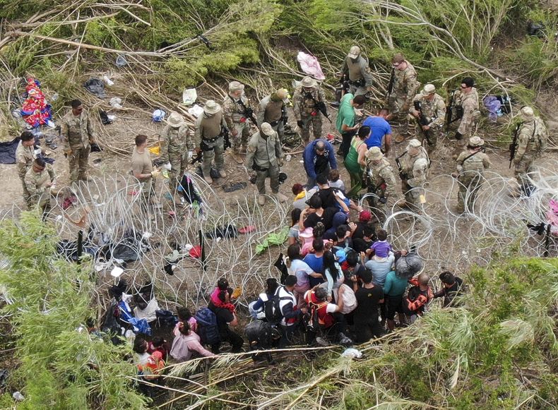Migrantes pasan a través de alambre de púas colocado a la orilla del río Bravo (Rio Grande en inglés), donde elementos de la Guardia Nacional de Texas les piden que no crucen. Los migrantes ingresaron a Estados Unidos para entregarse a las autoridades de inmigración el jueves 11 de mayo de 2023, en esta fotografía tomada desde Matamoros, México. Las restricciones al asilo relacionadas con la pandemia de COVID-19, conocidas como Título 42, están programadas a expirar el 11 de mayo. (AP Foto/Fernando Llano)