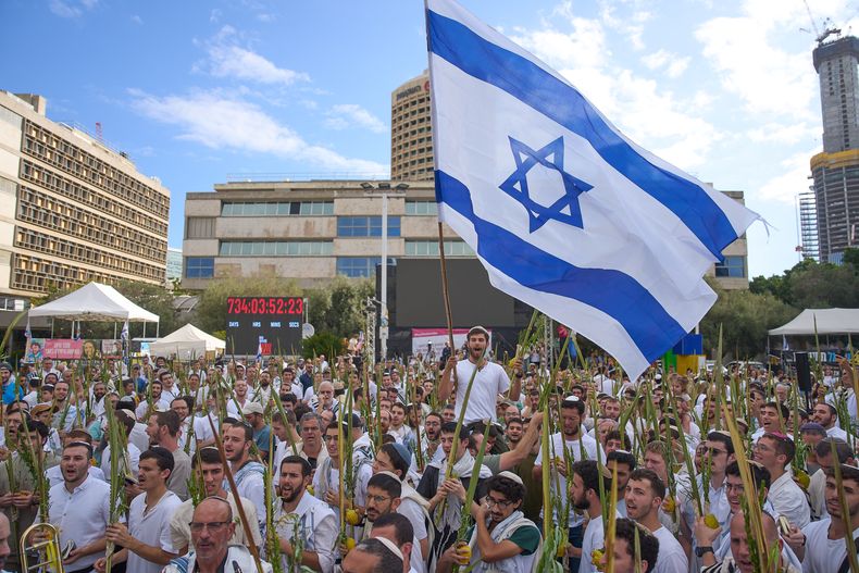 Cubiertos con mantos de oración, hombres bailan y sostienen los cuatro objetos utilizados como símbolo en la festividad judía de Sucot, en la llamada Plaza de los Rehenes tras el anuncio de que Israel y Hamás cerraron la primera fase del plan de paz para detener la guerra en Gaza, en Tel Aviv, Israel, el 10 de octubre de 2025. (AP Foto/Ariel Schalit)