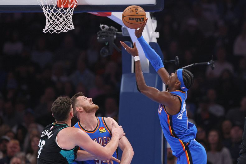 Shai Gilgeous-Alexander, escolta del Thunder de Oklahoma City, a la derecha, lanza junto al pívot de los Trail Blazers de Portland, Donovan Clingan, a la izquierda, y el pívot del Thunder, Isaiah Hartenstein, durante la primera mitad de un juego de baloncesto de la NBA, el domingo 23 de noviembre de 2025, en Oklahoma City. (AP Photo/Nate Billings)