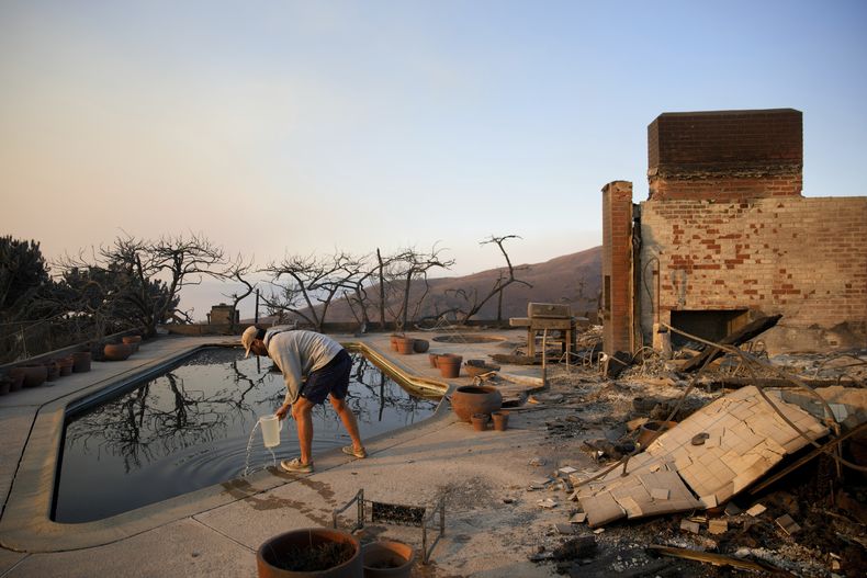 Garrett Yost saca agua de una piscina mientras revisa las propiedades de su vecino, arrasadas por el fuego, tras un devastador incendio en el vecindario Pacific Palisades de Los Ángeles, el 10 de enero de 2025. (AP Foto/John Locher)