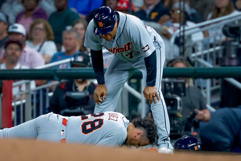 Javier Báez (28), de los Tigres de Detroit, reacciona tras lesionarse la pierna derecha mientras corría hacia la primera base en un rodado contra los Bravos de Atlanta, mientras el coach de primera base de los Tigres, Anthony Sanders (77), observa durante la quinta entrada de un partido de béisbol, el martes 28 de abril de 2026, en Atlanta. (AP Foto/Erik S. Lesser)