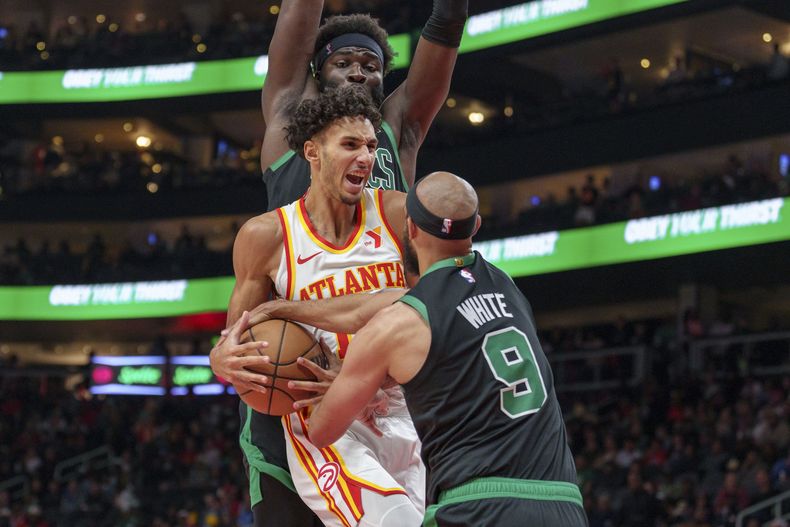 El alero de los Hawks de Atlanta, Zaccharie Risacher (10), intenta conducir hacia la canasta, pero el escolta de los Celtics de Boston, Derrick White (9), y el pívot Neemias Queta lo detienen durante la primera mitad, el lunes 4 de noviembre de 2024, en Atlanta. (AP Foto/Jason Allen)
