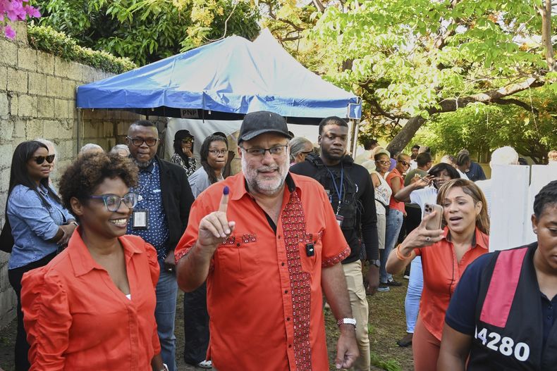 Mark Jefferson Golding (al centro), líder opositor, presidente del Partido Nacional del Pueblo y candidato a primer ministro, muestra su dedo marcado en señal de que votó durante las elecciones generales en una casilla electoral, el miércoles 3 de septiembre de 2025, en Kingston, Jamaica. (Foto AP/Collin Reid)