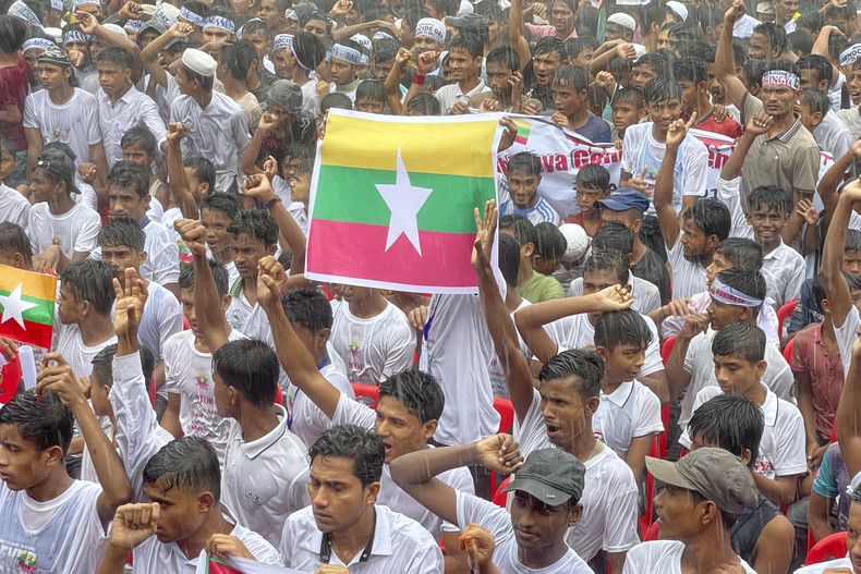 ARCHIVO - Refugiados rohinyas se reúnen bajo la lluvia con una bandera de Myanmar, en el centro, para reclamar un regreso seguro al estado de Rakhine en Myanmar, en el séptimo aniversario de su éxodo masivo en el campo de refugiados de Kutupalong en el distrito de Coxs Bazar, Bangladesh, el 25 de agosto de 2024. (AP Foto/Shafiqur Rahman, Archivo)