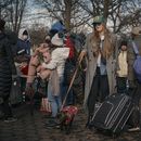 Una mujer pasea a su perro mientras migrantes recogen ropa distribuida por grupos de ayuda cerca del Centro de Asistencia al Migrante en la Escuela Primaria Santa Brígida, el sábado 20 de enero de 2024, en Nueva York. (AP Foto/Andres Kudacki)