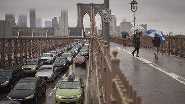 Personas con sombrillas caminan a un costado de los vehículos por el Puente de Brooklyn, luego de las fuertes lluvias del viernes 29 de septiembre de 2023, en Nueva York. (AP Foto/Andres Kudacki)