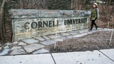 Una mujer camina junto a una placa de la Universidad de Cornell en el campus de la escuela de la Ivy League en Ithaca, Nueva York, el viernes 14 de enero de 2022. (AP foto/Ted Shaffrey, archivo)
