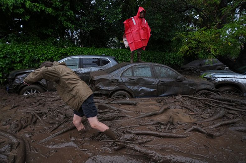 Un hombre está de pie sobre el techo de un automóvil mientras otro camina por aguas lodosas tras las fuertes lluvias que provocaron inundaciones repentinas en la comuna de Las Condes, en Santiago de Chile, el jueves 8 de octubre de 2026. (Foto AP/Esteban Félix)